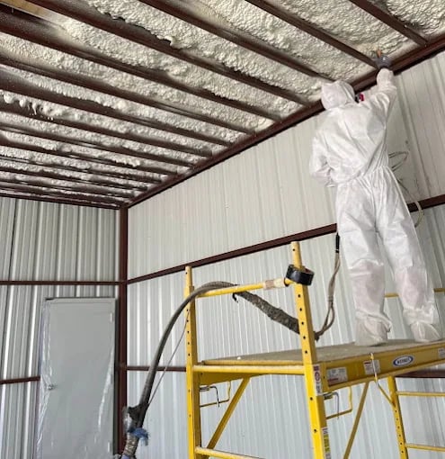 Worker in white protective suit installing insulation on industrial metal ceiling