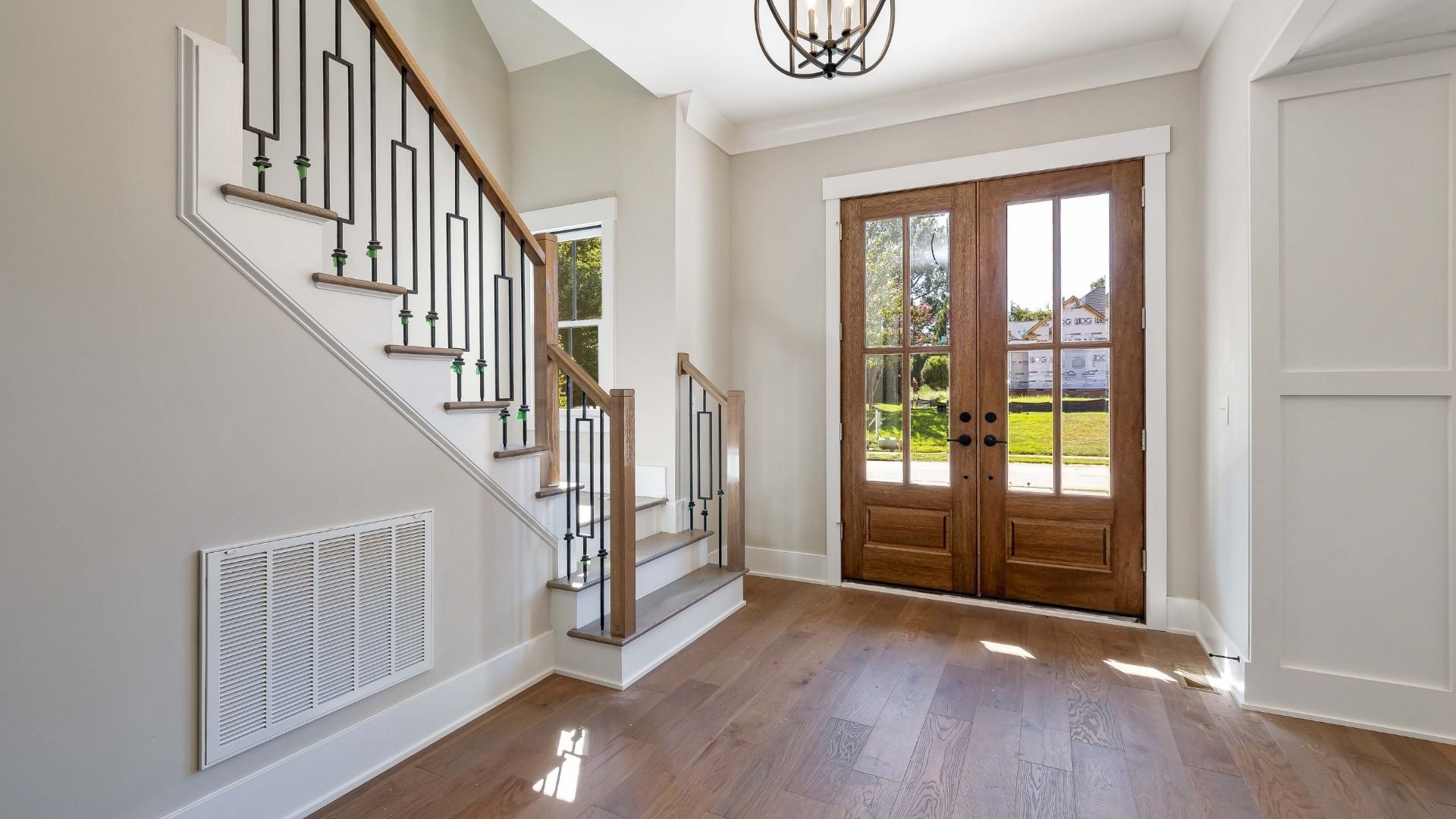 Modern foyer with wooden stairs, metal railing, double doors, and hardwood floors.