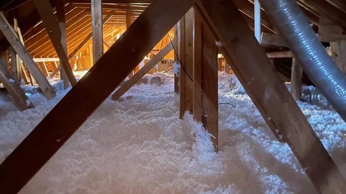 Attic interior with exposed wooden beams, insulation, and warm lighting from above.