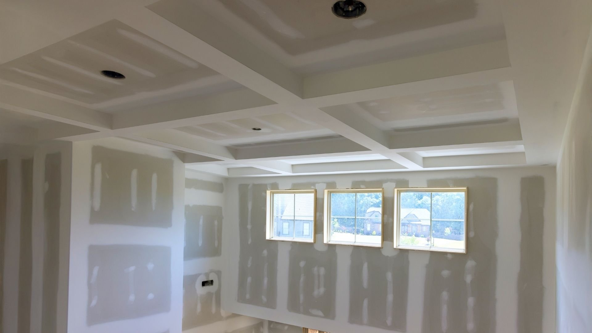 Unfinished interior with drywall, coffered ceiling, recessed lights, and large windows overlooking landscape